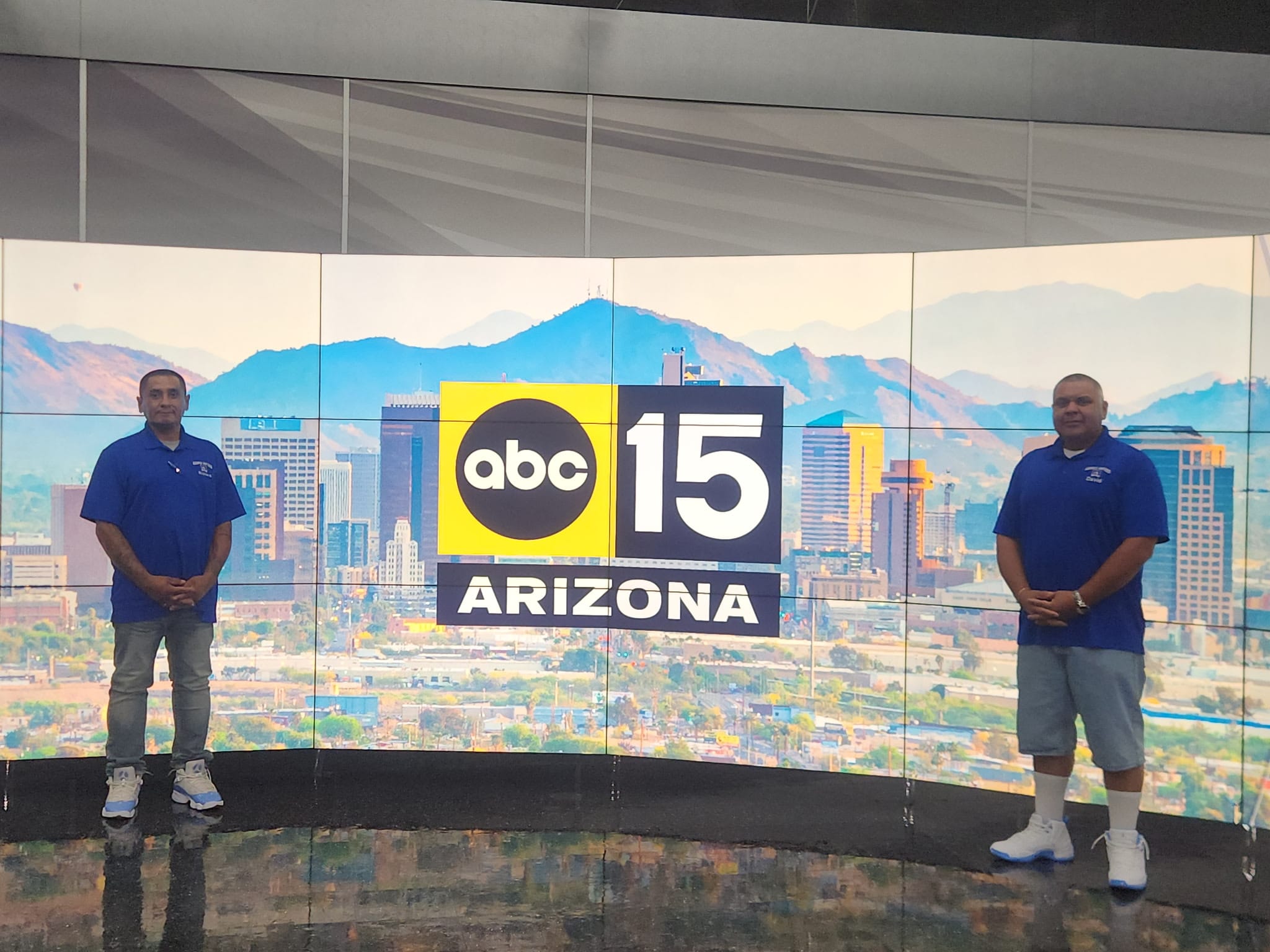 Garcia Movers owners standing beside the ABC15 Arizona logo on the studio video wall in Phoenix