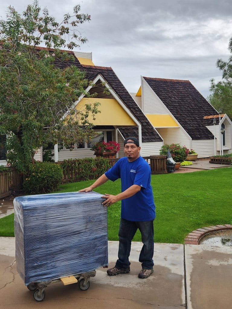 A Garcia mover rolling a shrink-wrapped cart across the lawn to the truck