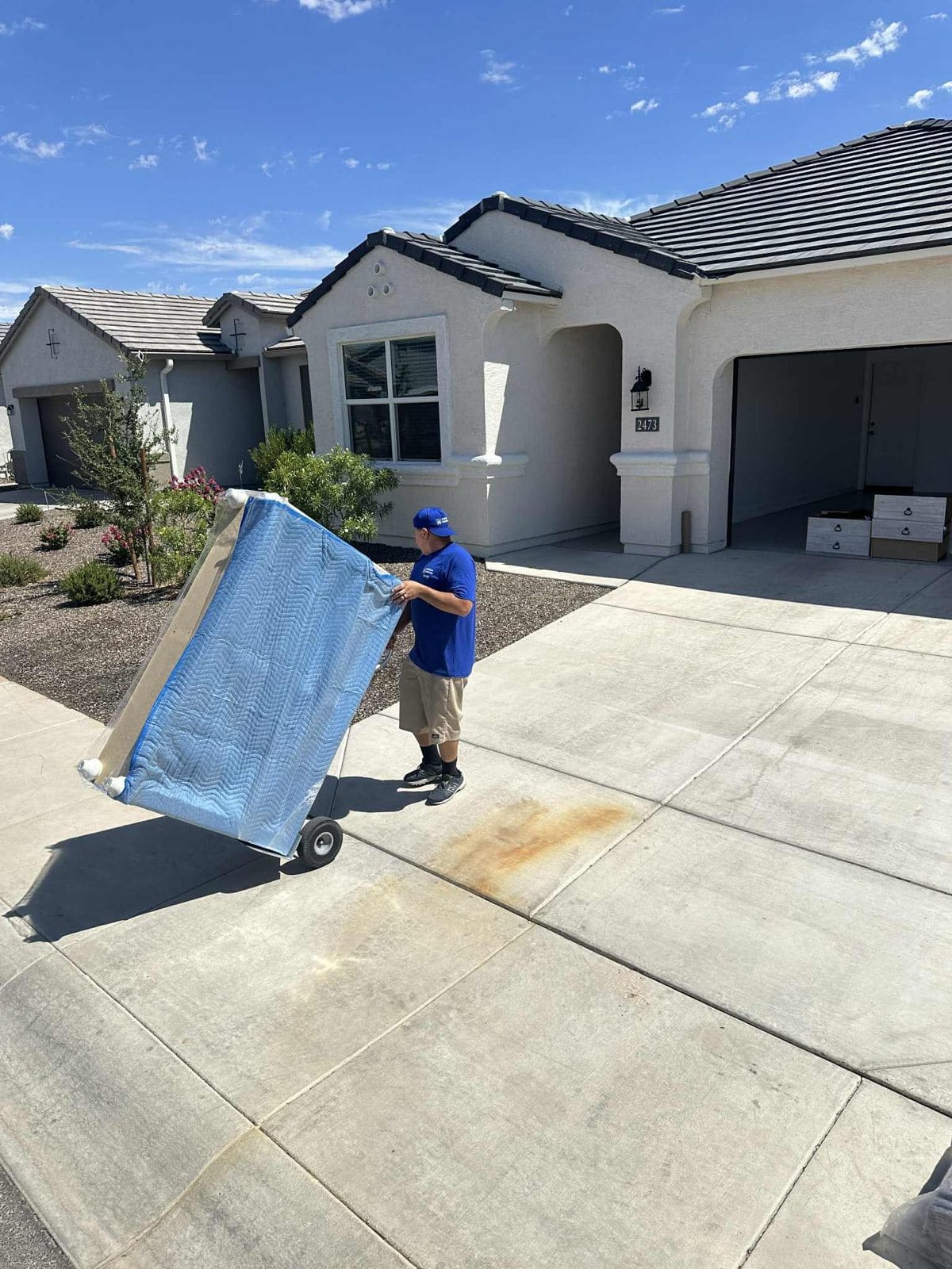 A Garcia mover rolling a blanket-wrapped piece up the driveway of a new home